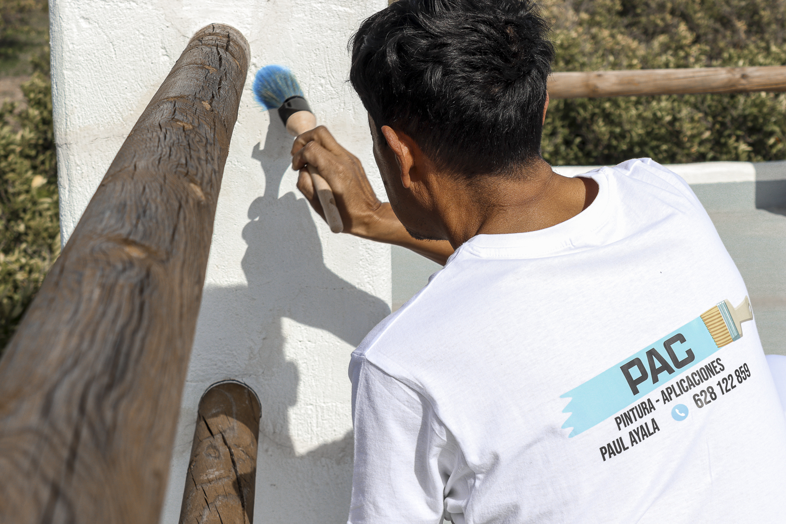 Pintor trabajando en una barandilla junto a una pared blanca