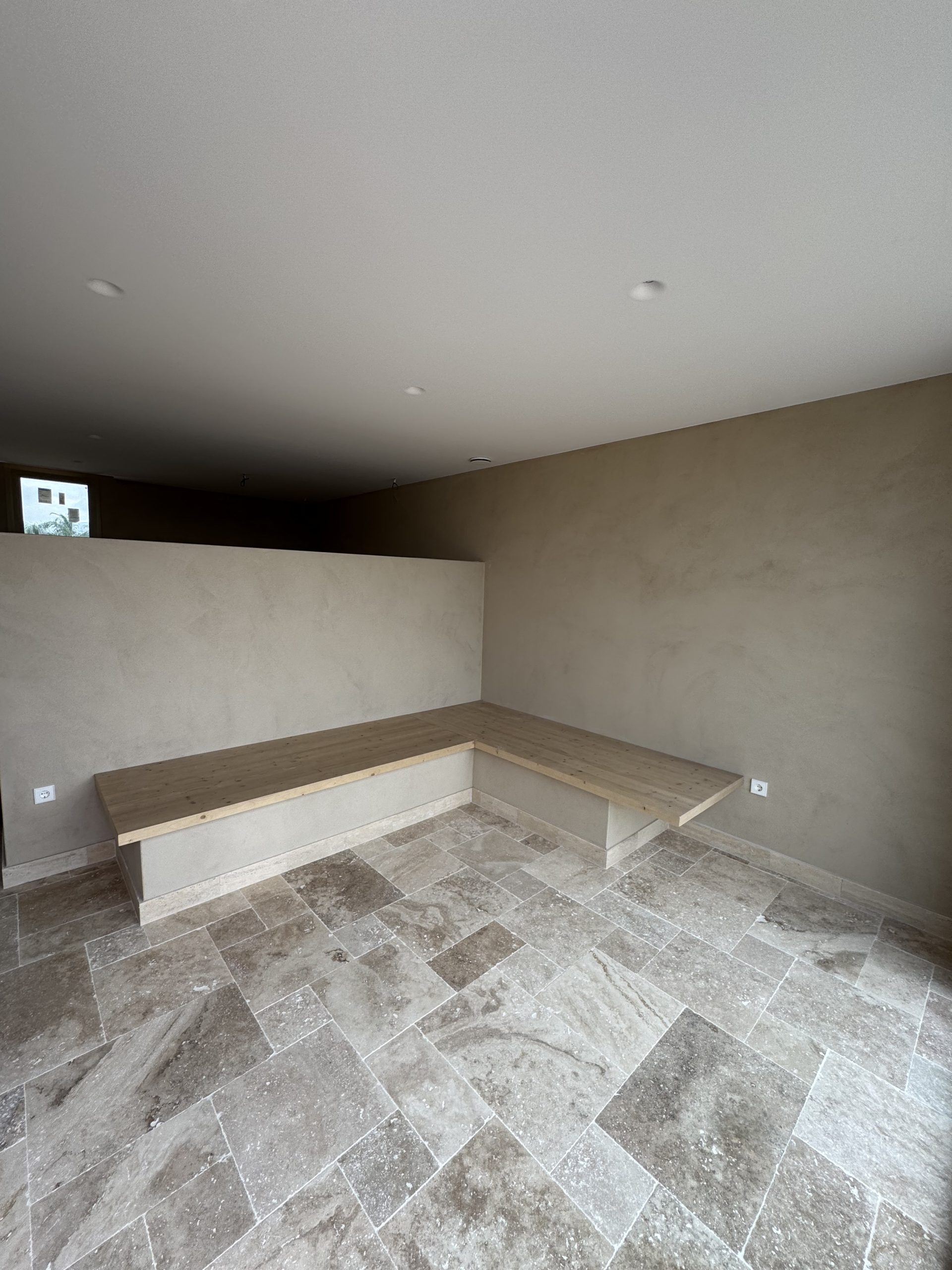 Interior con paredes de acabado mineral, banco de madera y pavimento de piedra